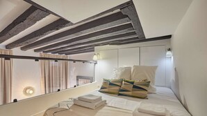 A bedroom with a sloped ceiling, a bed with white linens, pillows, and a bedside lamp. - Superb Apartement Center of Paris Le Marais (Paris)