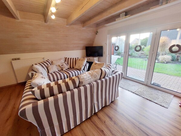 Sala de estar com sofá listrado, televisão e vista para o exterior através de uma porta de vidro.