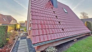 A house with a steep red roof, a visible chimney, and a small window.