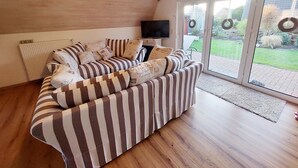 A living room with a striped sofa, a television, and a view of the garden through glass doors.
