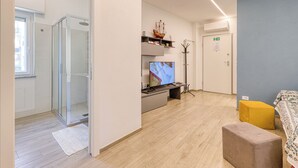 Een moderne woonkamer met een douchecabine van glas, een flatscreen televisie, een kleine tafel en een bank.
