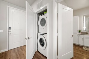 A laundry room with two stacked washing machines, a door with a lock, and a wooden floor.