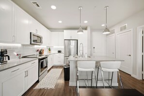 A modern kitchen with white cabinets, stainless steel appliances, and a central island with bar stools. - MCK211 | McKinney Corporate 2BD | Pool | Workspace (McKinney)