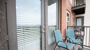 Ein Balkon mit Metallgeländern, einer Glastür mit Jalousien und zwei blauen Stühlen.