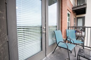 A balcony with metal railings, a glass door with blinds, and two blue chairs. - MCK211 - Apt|Patio|15mi to Toyota Stadium|Sleeps 4 (McKinney)