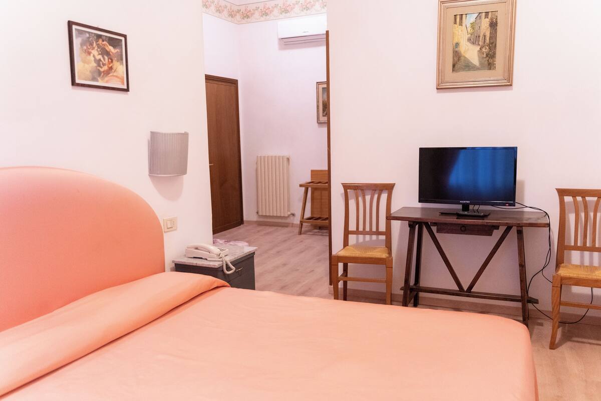 Ein Schlafzimmer mit einem Bett, einem Schreibtisch mit Fernseher und zwei Stühlen.