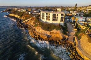 A coastal hotel with a balcony, located near the sea, surrounded by residential buildings.