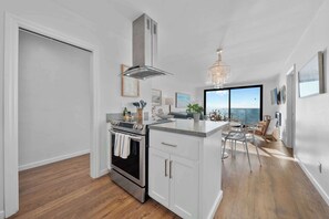 A modern kitchen with a stainless steel range, white cabinetry, and a large window offering a view.