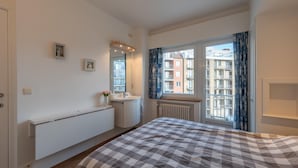 Un dormitorio con cama, ventana con cortinas, radiador y un cuadro pequeño en la pared.