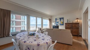 Un salón moderno con una mesa de comedor redonda, sofá blanco y grandes ventanales que dan al mar.