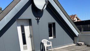 Un bâtiment gris avec une antenne parabolique, une porte, une fenêtre et une chaise en plastique blanche.