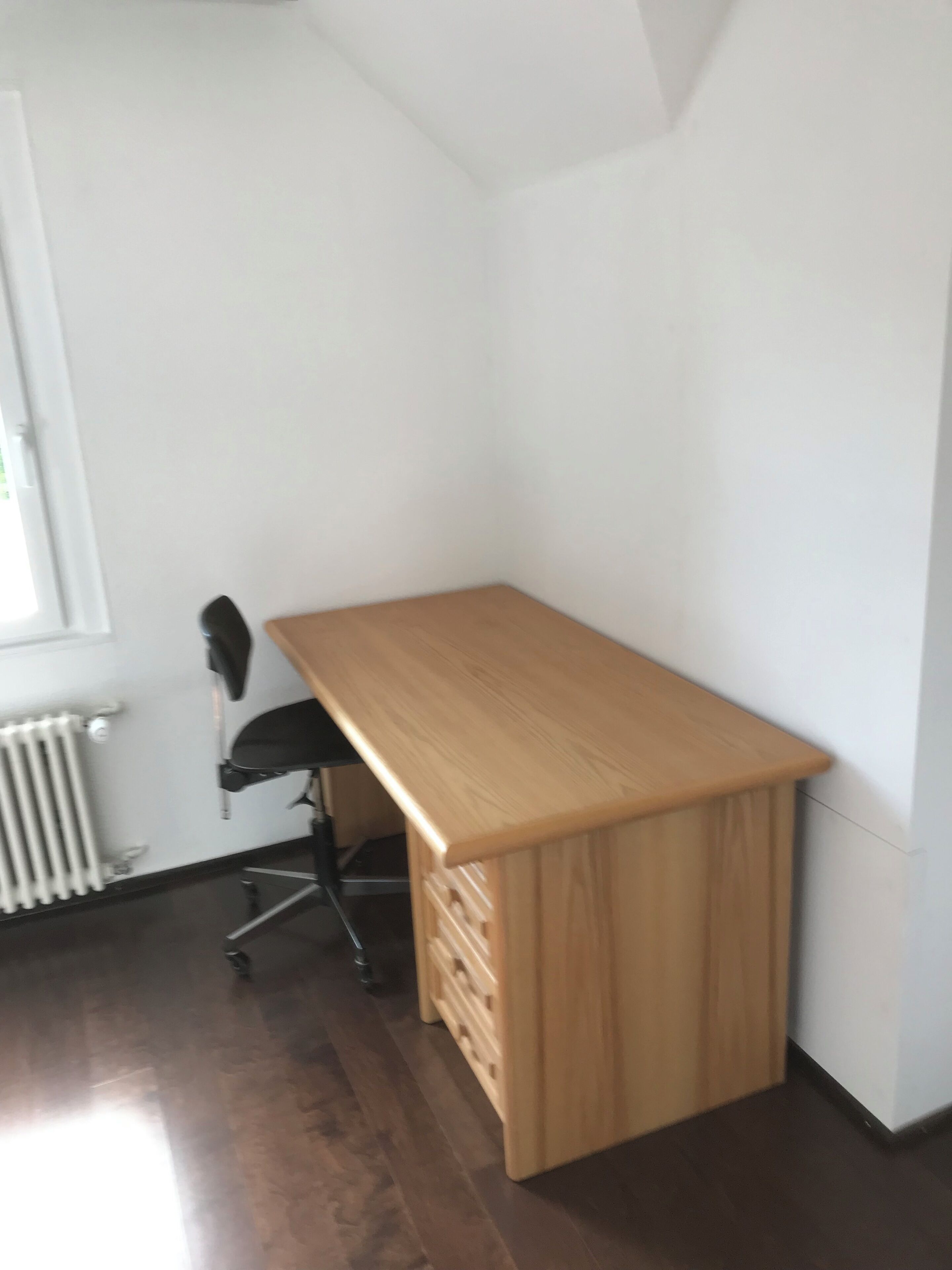 Une pièce d’angle avec un bureau en bois, un radiateur et une chaise.