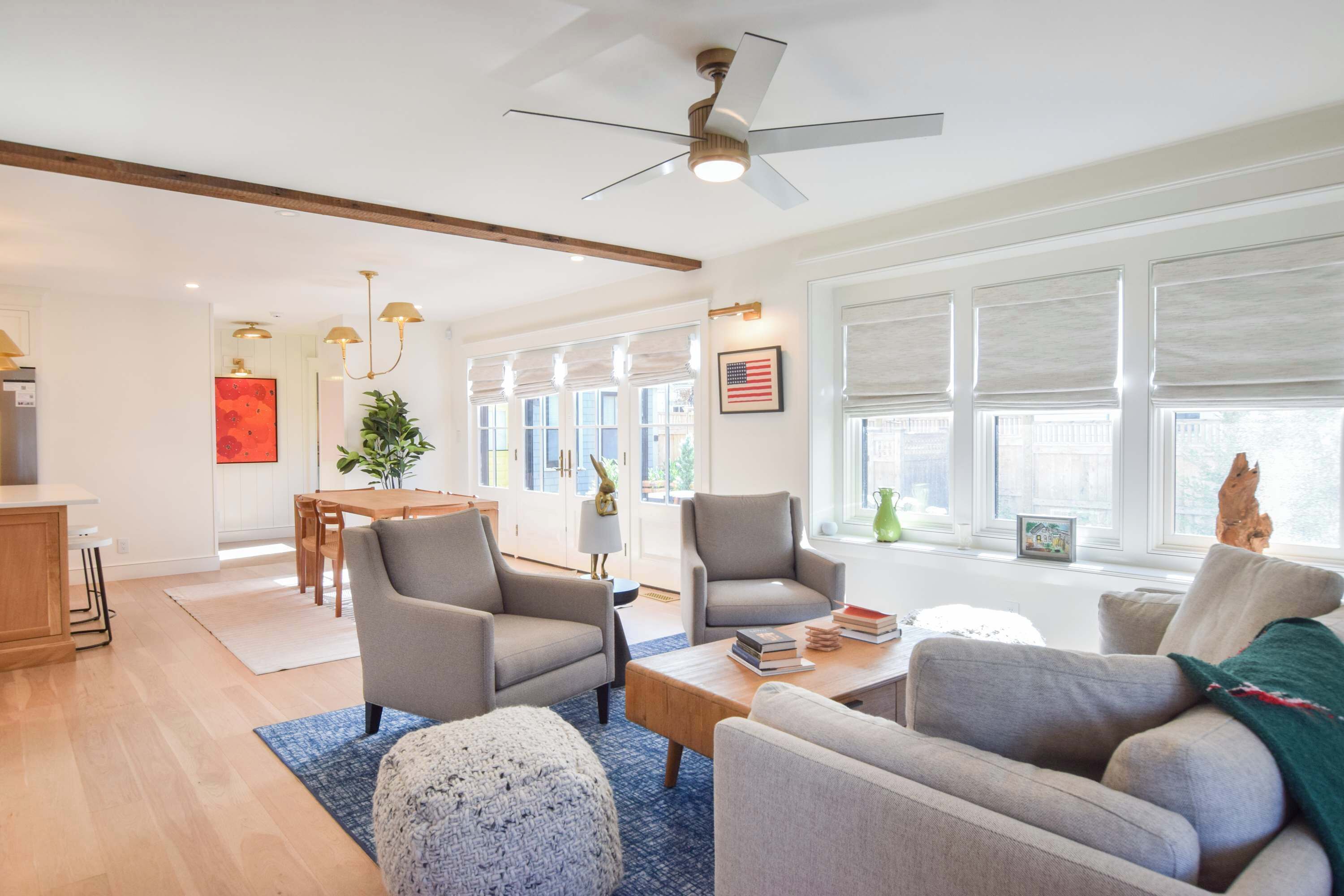 A spacious living room with a ceiling fan, a dining area with a wooden table and chairs, and large windows with blinds.