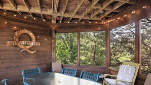 A covered outdoor seating area with a glass table and metal chairs, surrounded by wooden walls and large windows.