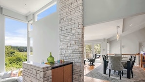 A modern kitchen with a stone accent wall, a dining area with a wooden table and chairs, and a view of the outdoors.