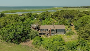 A large house surrounded by dense forest, with a view of the ocean in the background.