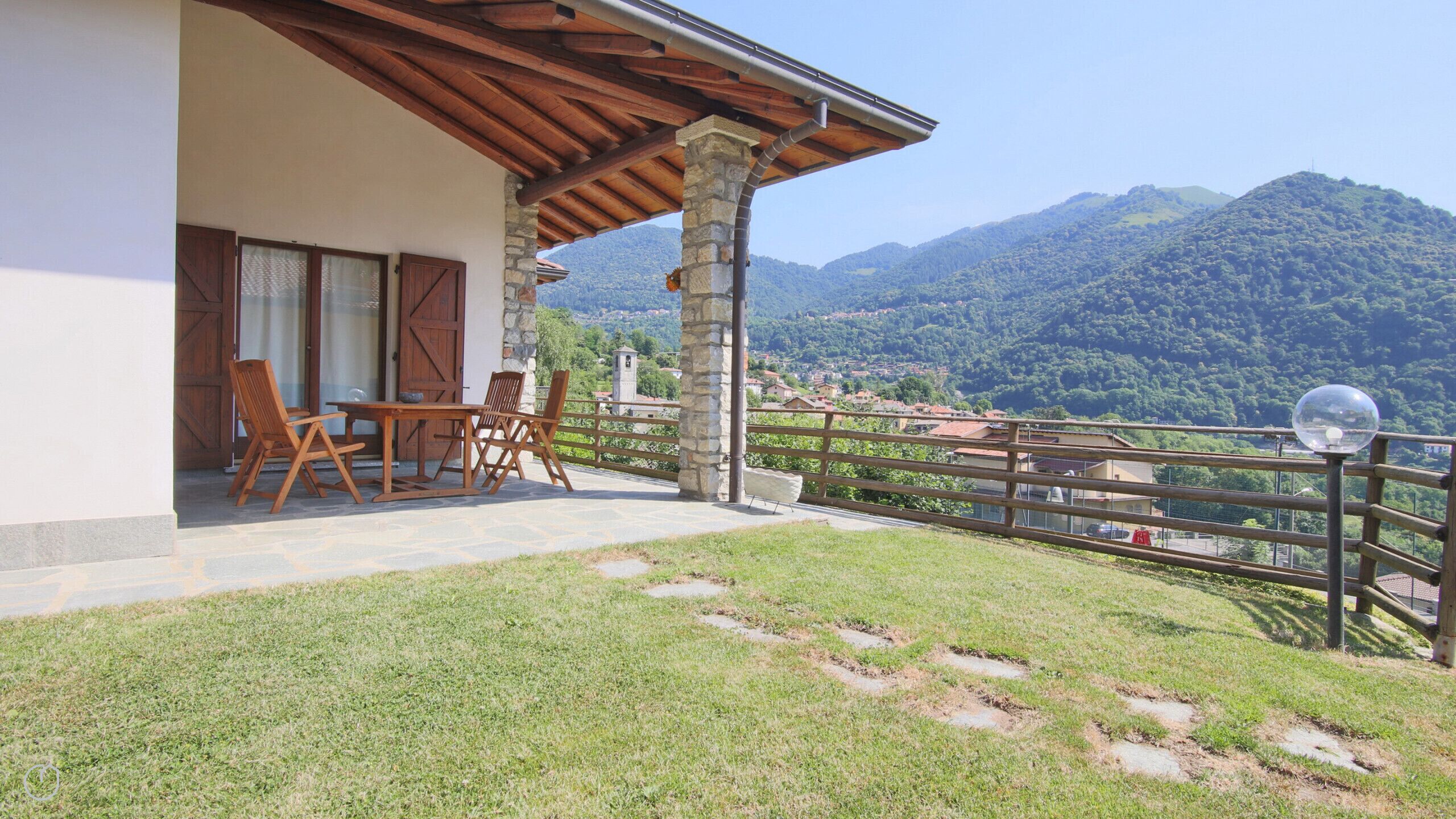Eine Terrasse mit Tisch und Stühlen, einer Steinsäule und Blick auf eine gebirgige Landschaft.