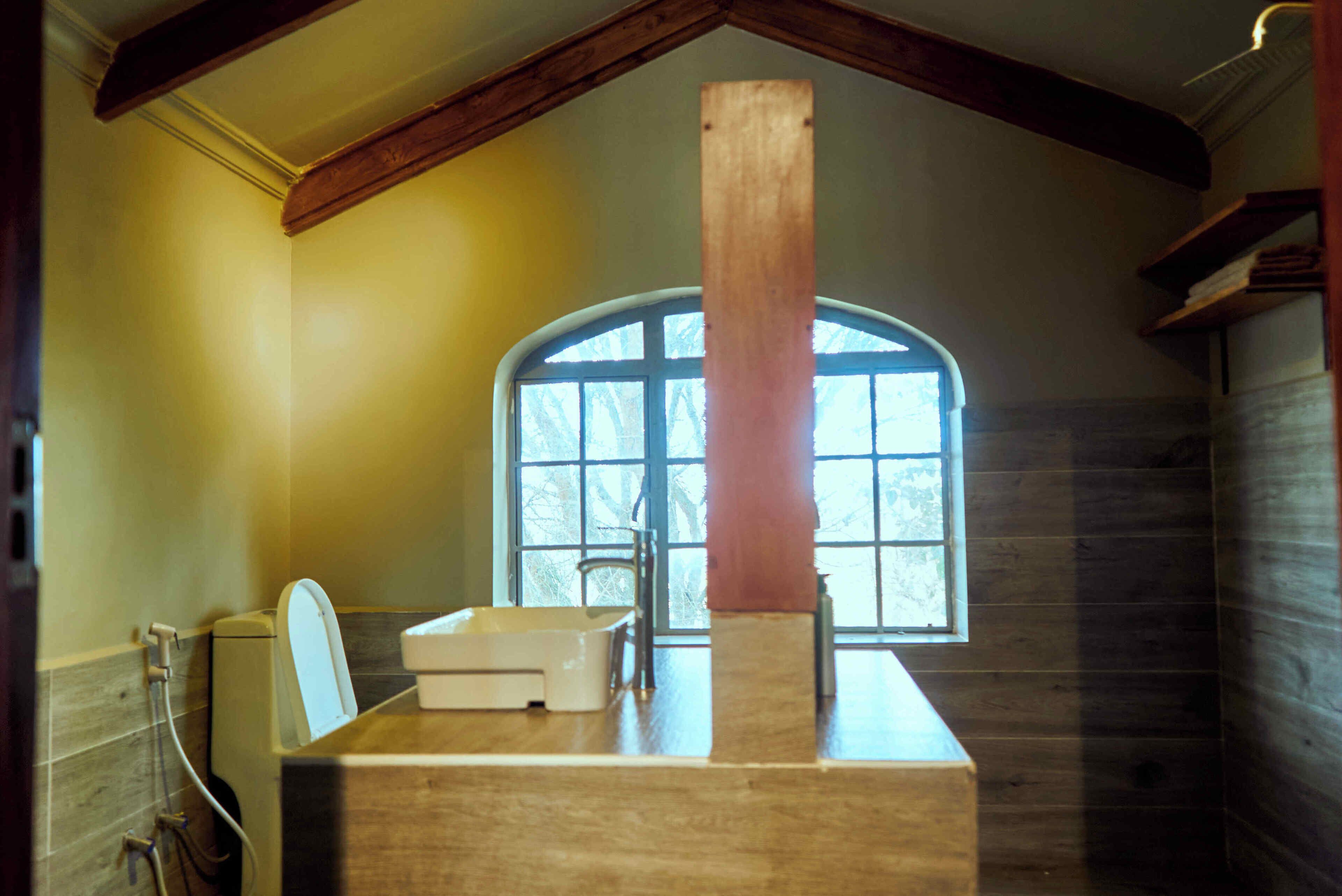 A bathroom with a wooden beam ceiling, a window with a view, a sink, and a toilet.