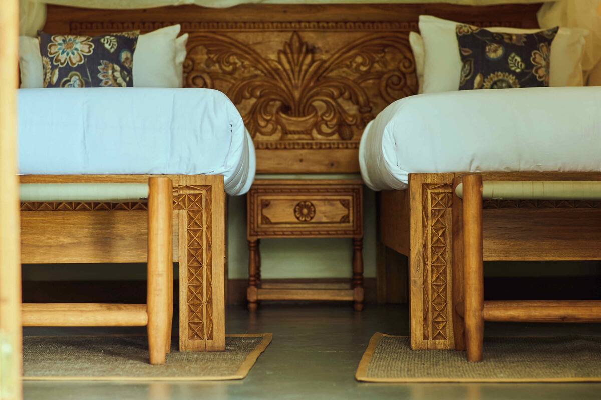 Two wooden beds with intricate carvings, a nightstand with a drawer, and a decorative headboard.