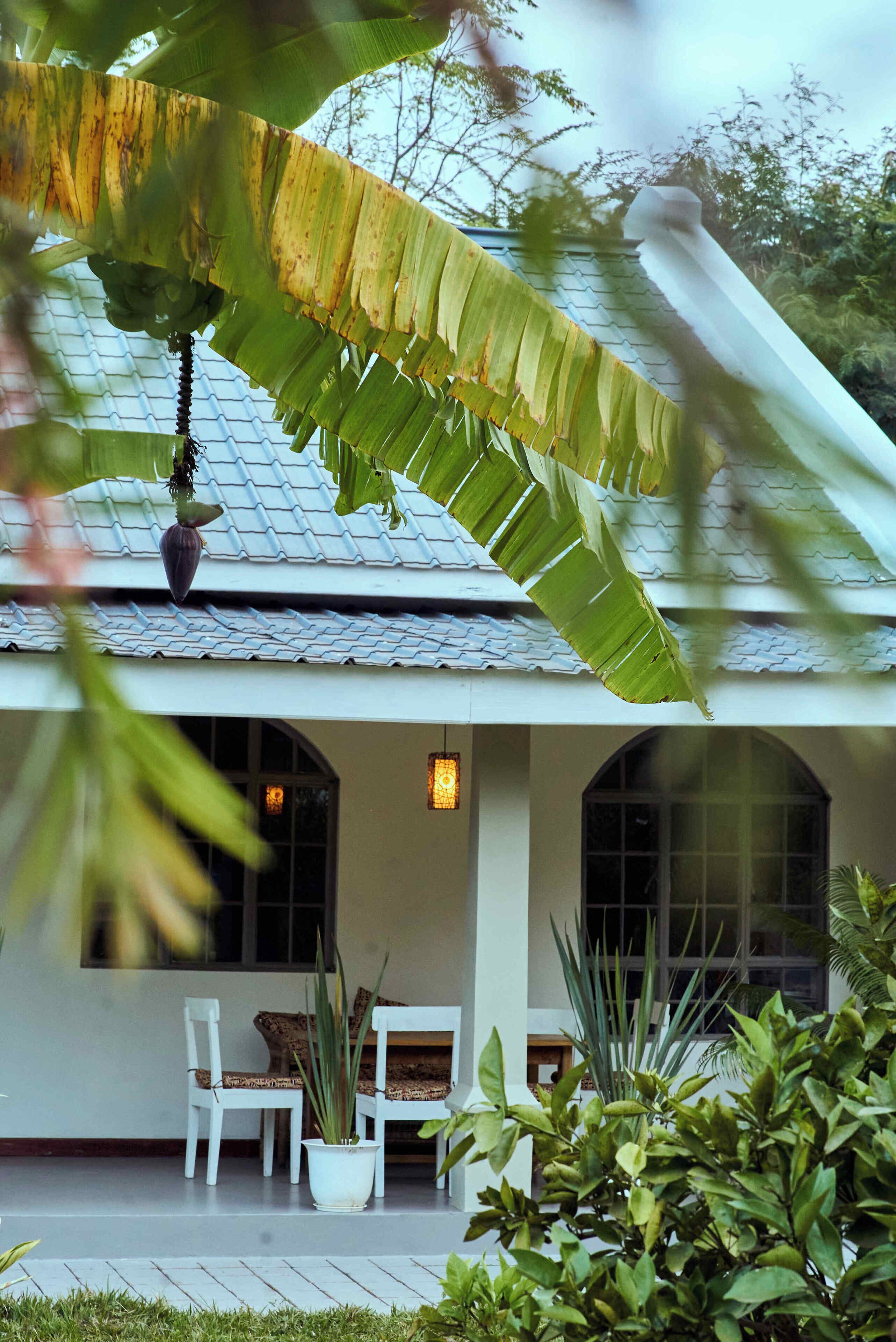 A house with a tiled roof, white walls, and a covered porch with two white chairs and a potted plant.