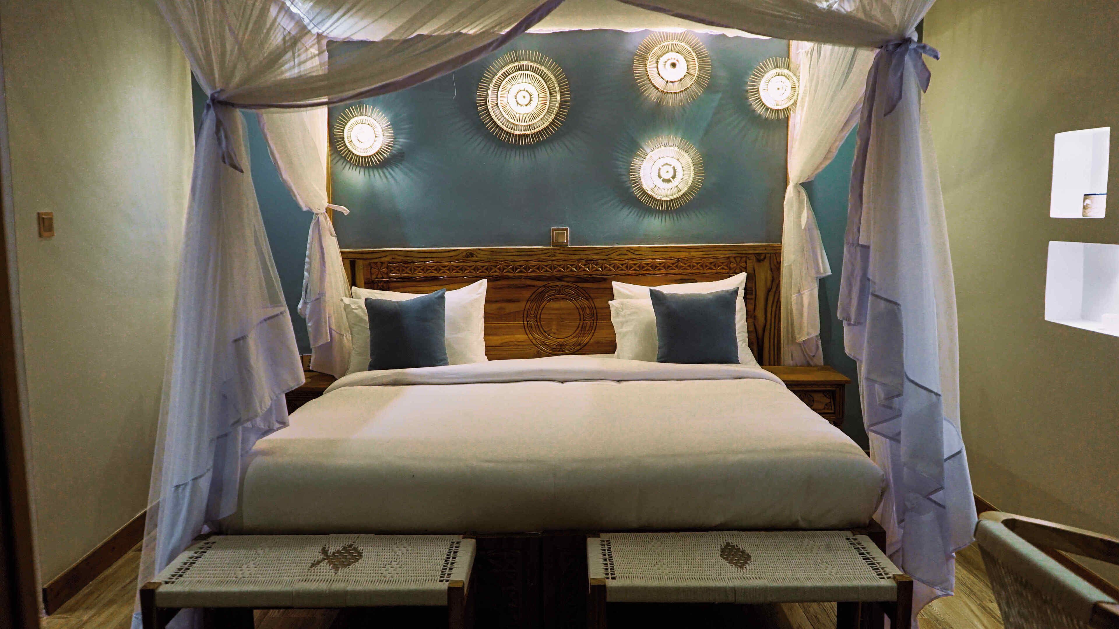 Una cama con dosel, cabecera con diseño circular y cuatro lámparas fijadas a la pared.