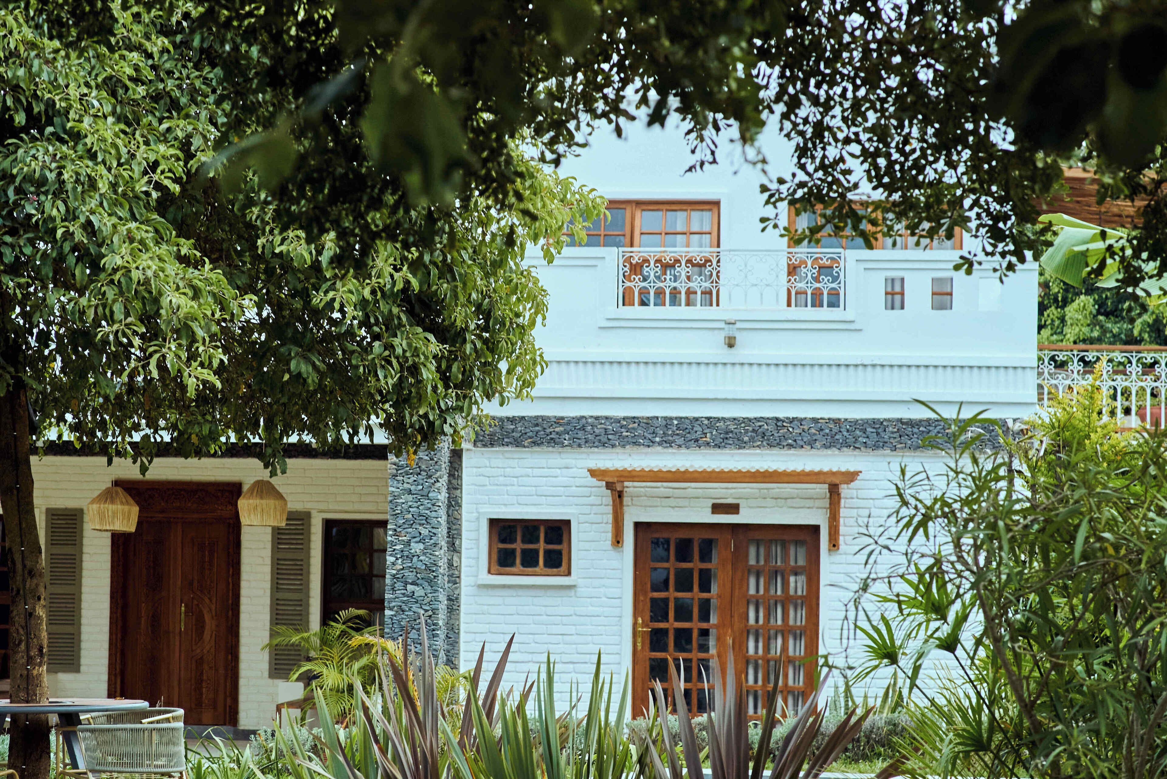 A white building with a wooden door and windows, surrounded by lush greenery.