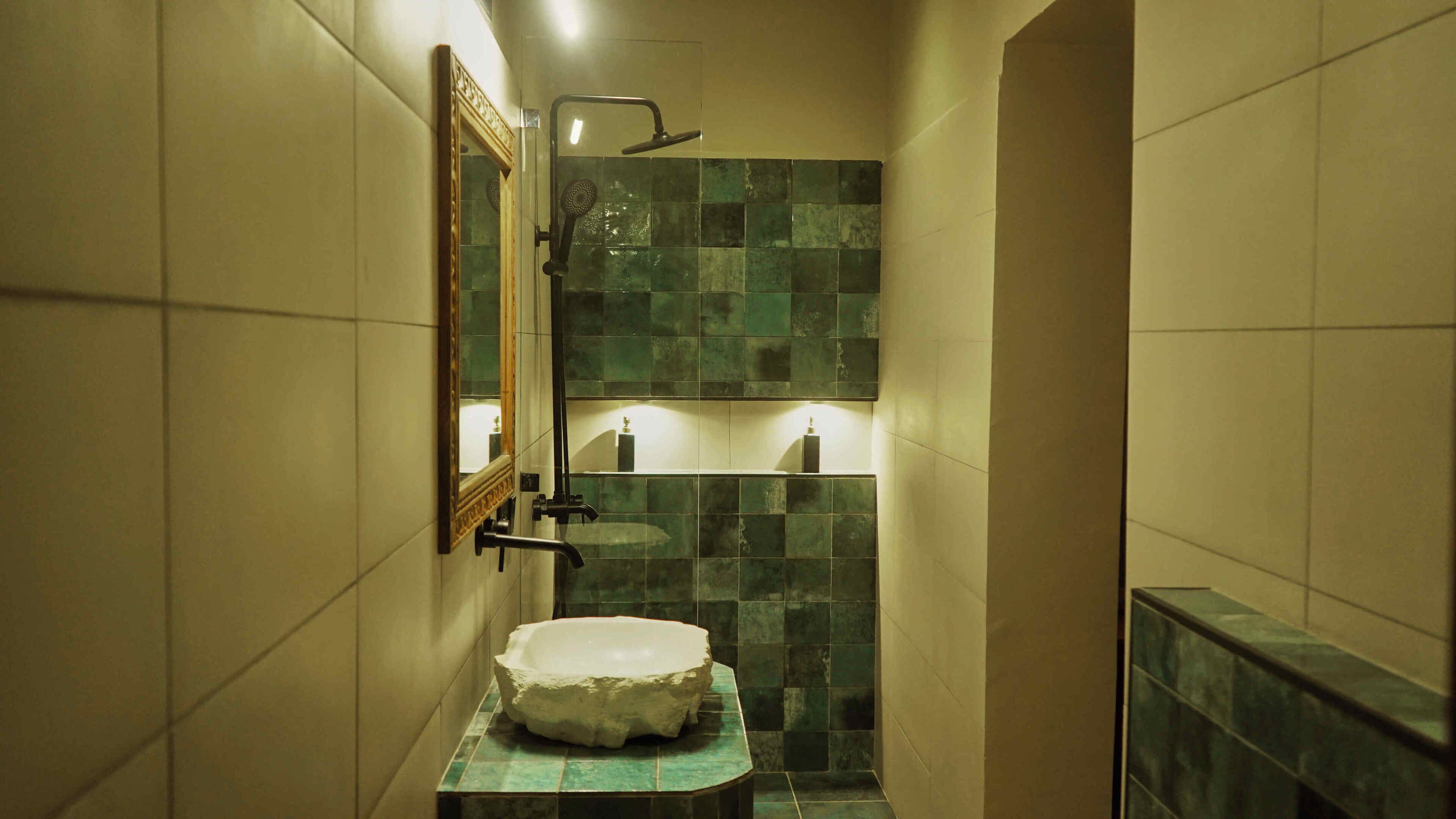 A narrow bathroom with a stone sink, a mirror, and a shower.