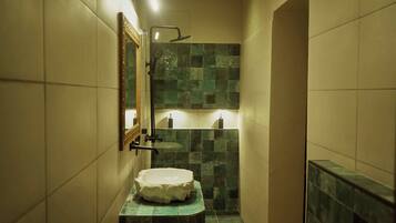 A narrow bathroom with a stone sink, a mirror, and a shower.