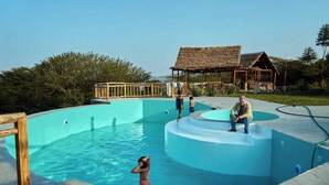 A swimming pool with a wooden deck and a thatched-roof structure. - Mateves Boutique Lodge  (Arusha)