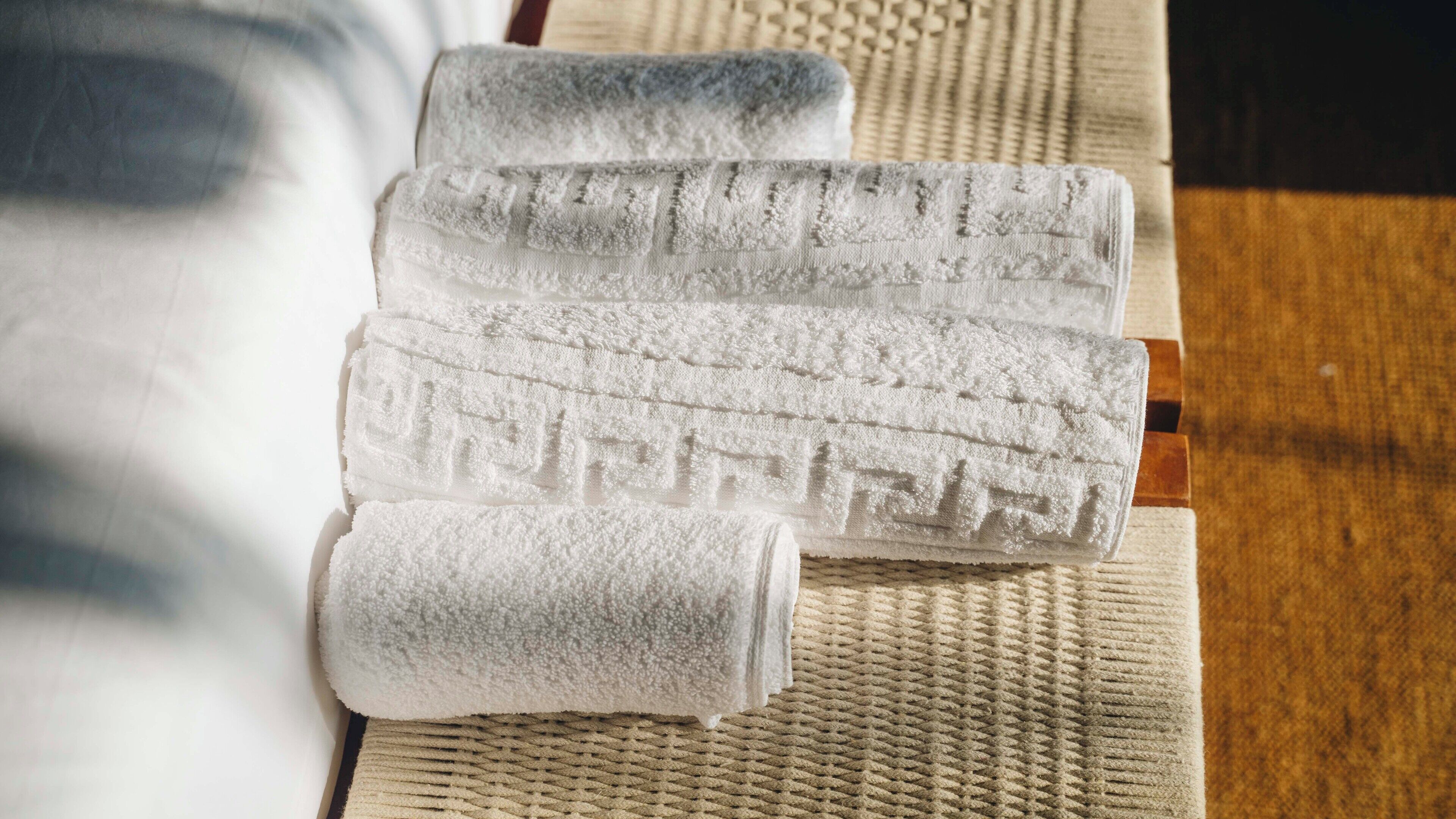 A set of white towels with a textured pattern, neatly folded on a woven mat.