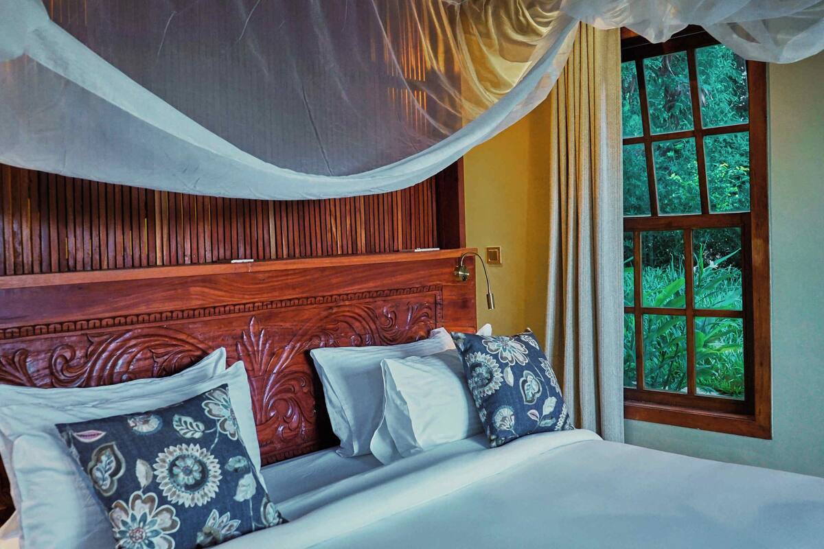 A bedroom with a wooden headboard, a canopy, and a window with a view of greenery.