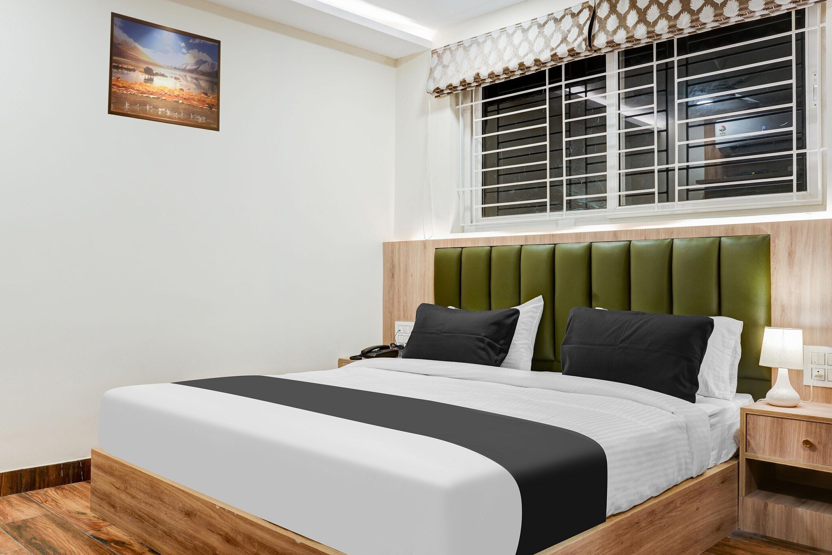A neatly arranged hotel room with a bed, a nightstand, a lamp, and a window with blinds.