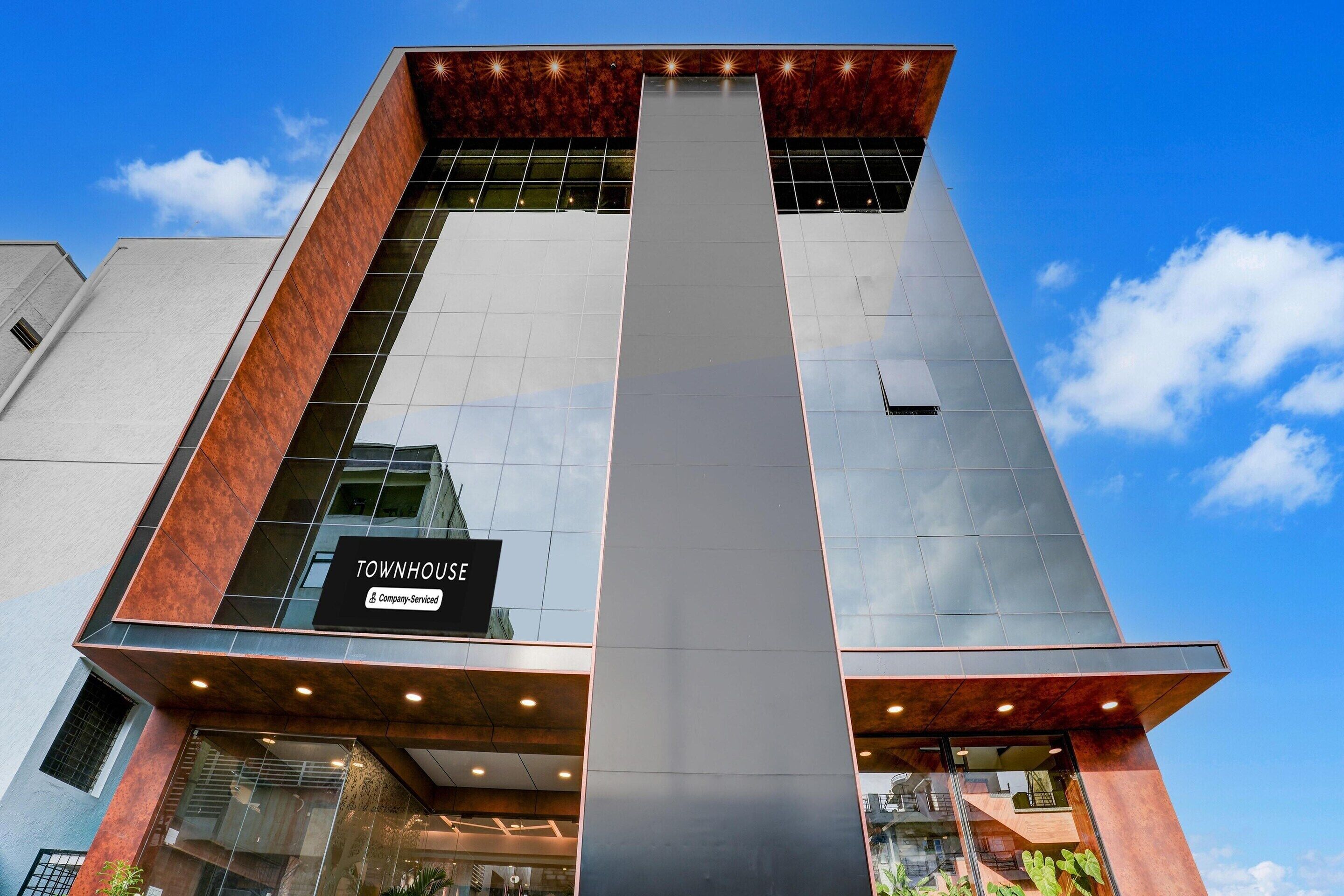 A modern building with a prominent vertical glass facade, a sign reading 'TOWNHOUSE & Company-Serviced,' and a clear blue sky in the background.