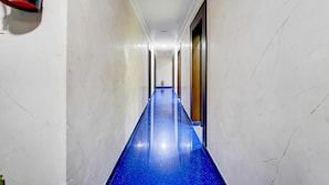 A hallway with a blue floor, white walls, and a ceiling light. - Super Hotel O Perungalathur (Chennai)