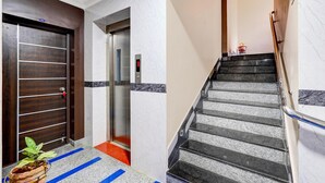 A hotel lobby with a wooden door, an elevator, and a staircase with a handrail. - Super Hotel O Perungalathur (Chennai)