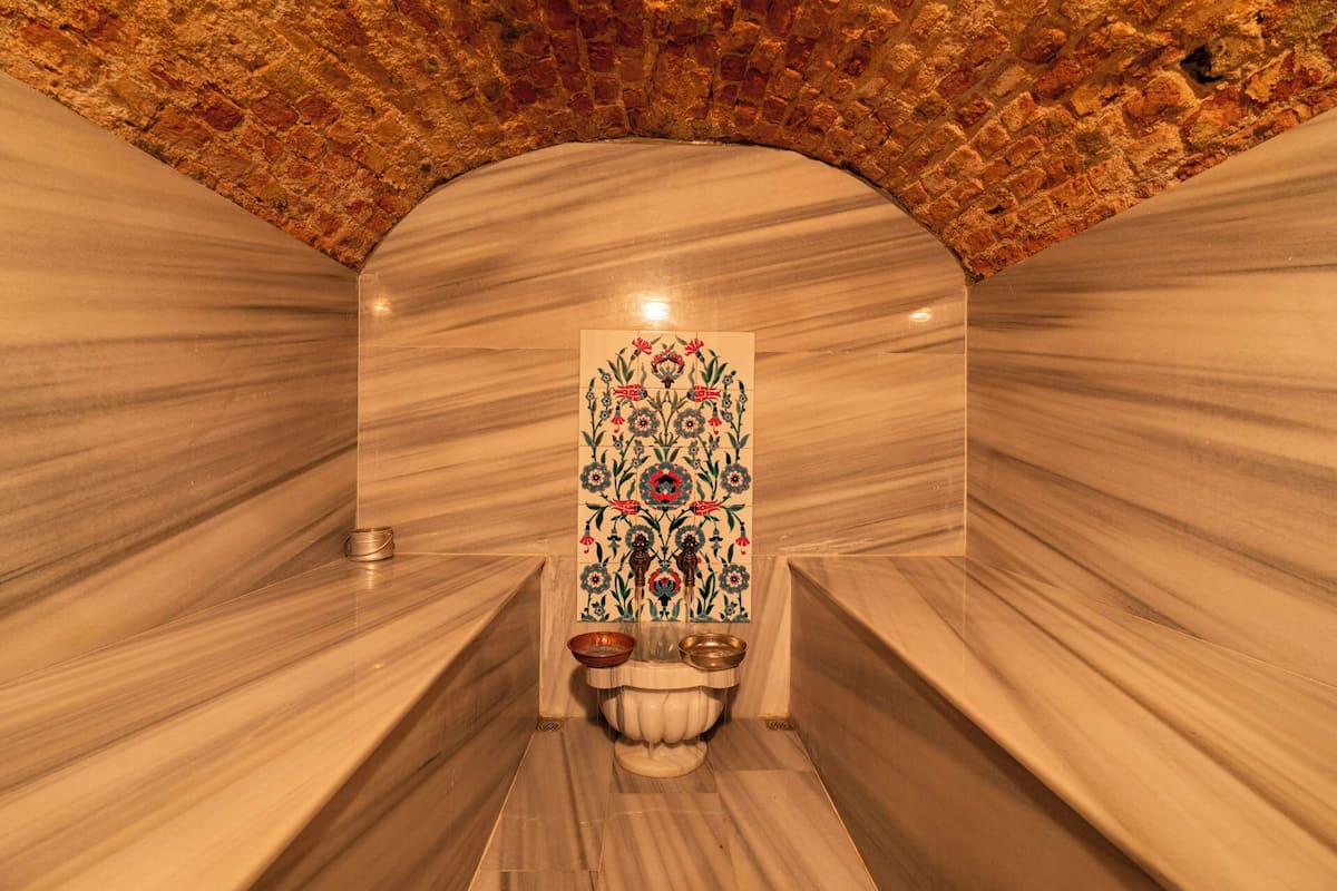 Um espaço de spa com paredes de mármore, um painel decorativo de azulejos e uma pequena pia com duas bacias.