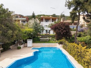 A swimming pool surrounded by lush greenery and a multi-story building with balconies.