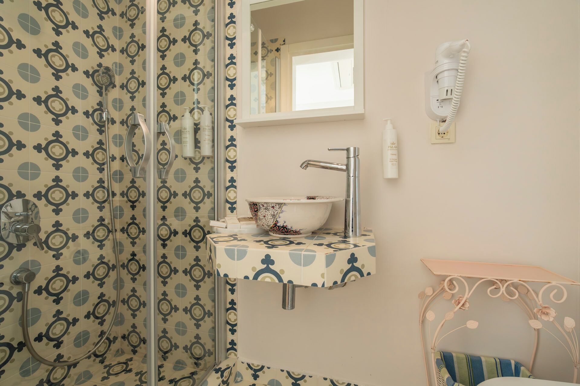 Une salle de bain avec un mur recouvert de carreaux décoratifs, un lavabo sur pied agrémenté d’un miroir décoratif, une douchette à main et un téléphone fixé au mur.