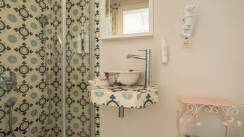 Une salle de bain avec un mur recouvert de carreaux décoratifs, un lavabo sur pied agrémenté d’un miroir décoratif, une douchette à main et un téléphone fixé au mur.