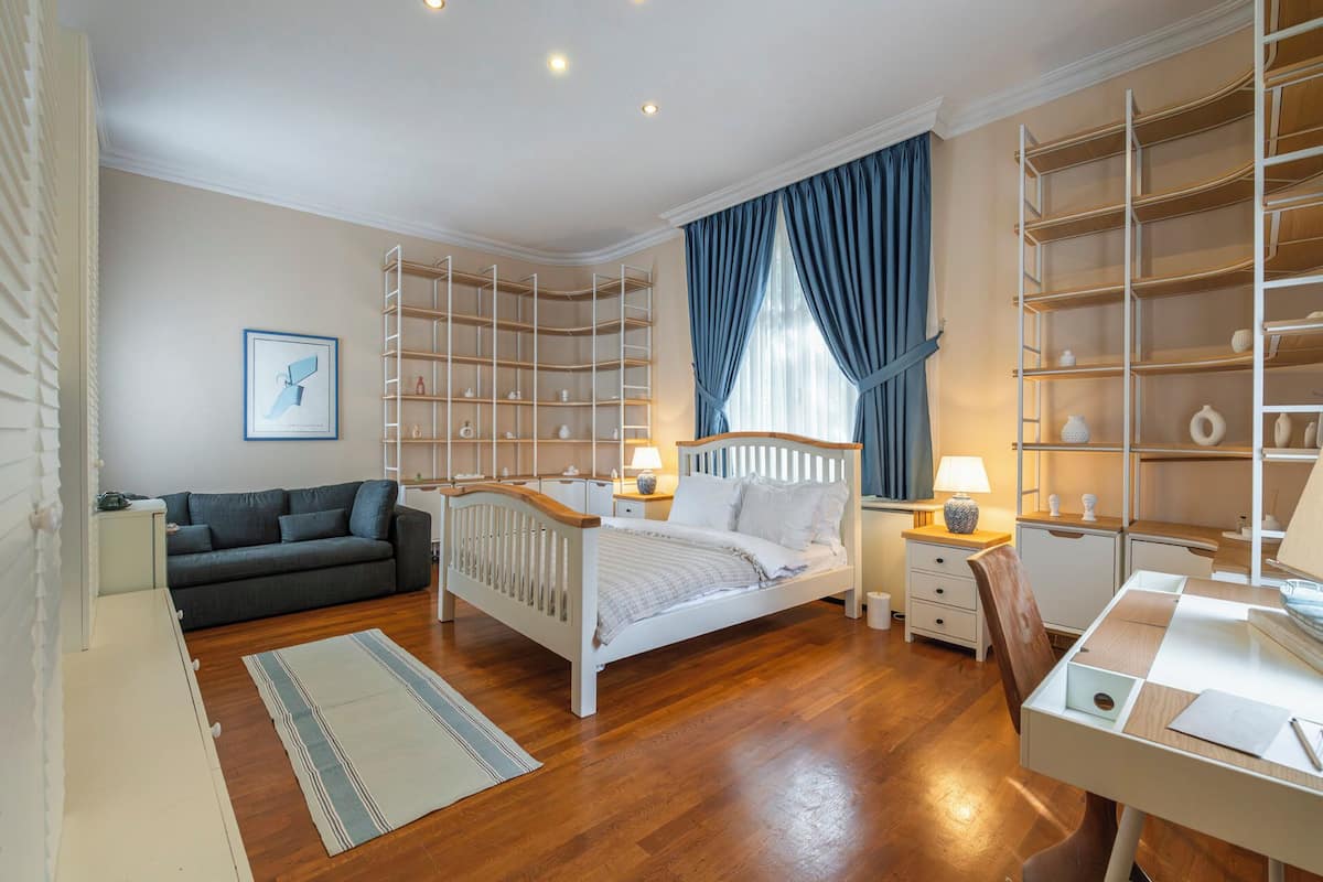 Quarto com cama, escrivaninha, poltrona, sofá e estantes embutidas.