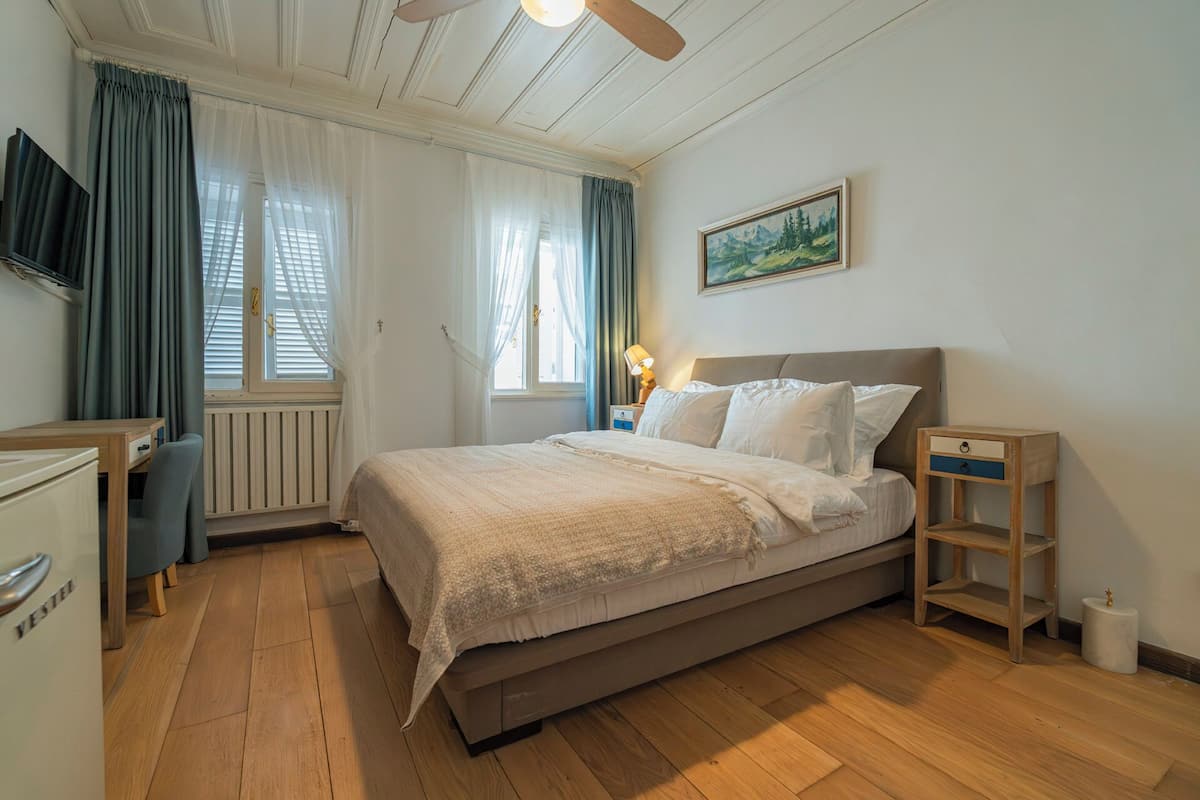Quarto com cama, escrivaninha, cadeira, abajur e um quadro na parede.