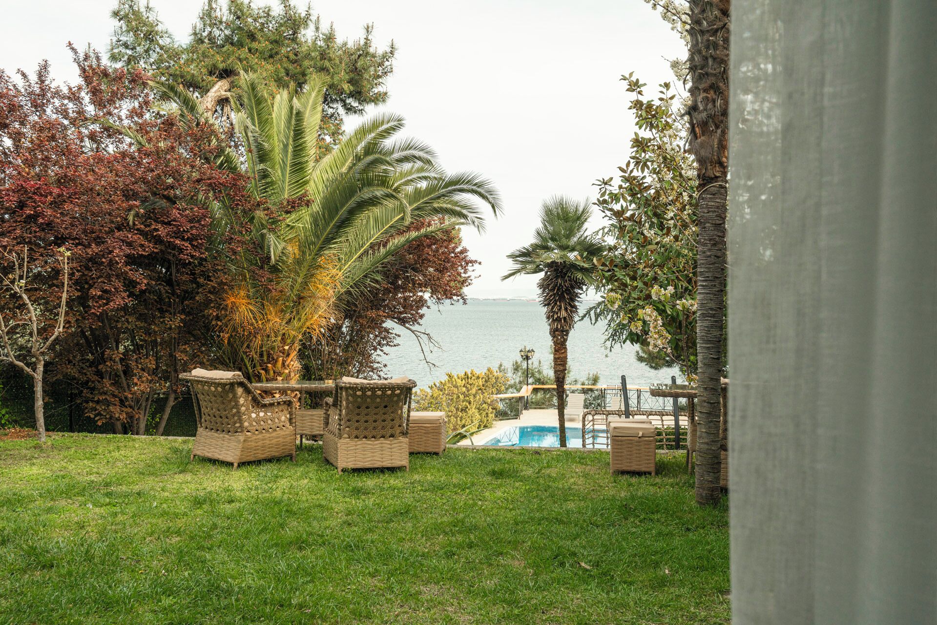 A poolside area with wicker furniture and a view of the sea.