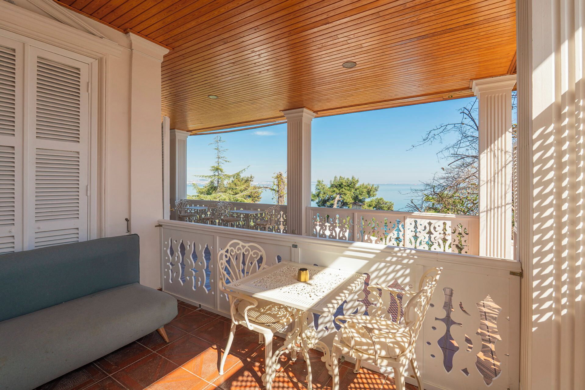 Un patio cubierto con una mesa y sillas blancas, un banco azul y vistas al mar.