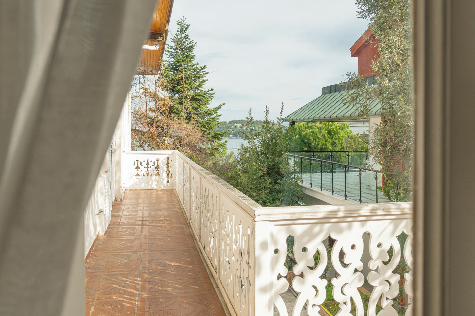 A balcony with a patterned floor, white decorative railing, and a view of a lake and buildings.