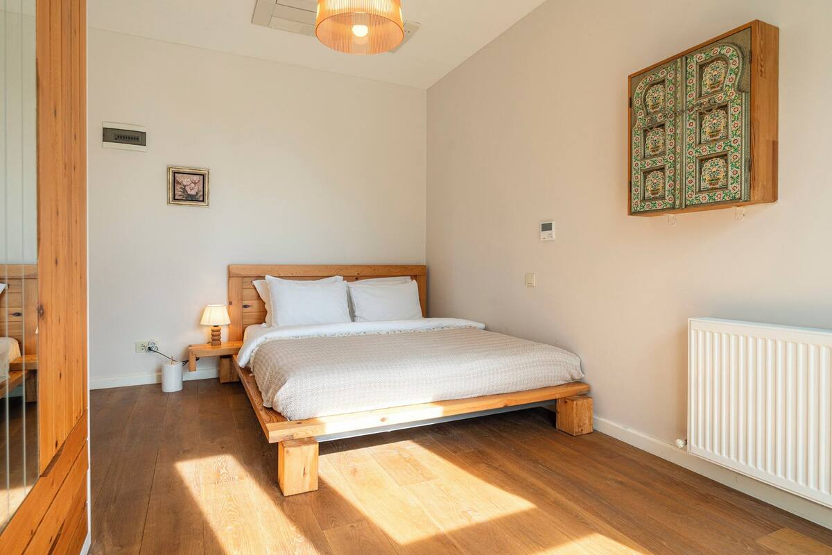 Quarto com cama de madeira, mesa de cabeceira, luminária e radiador.