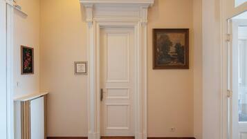 Un pasillo con una puerta blanca, un cuadro enmarcado y una pequeña estantería con un objeto enmarcado.