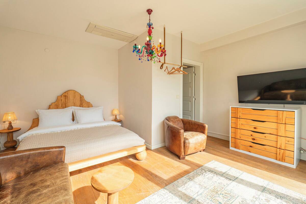Quarto com cama, penteadeira de madeira, televisão, cadeira e lustre.