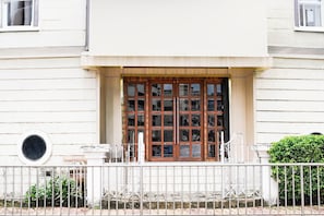 Un edificio con un amplio ventanal de madera, un ventanuilla circular pequeña y una cerca metálica al frente.