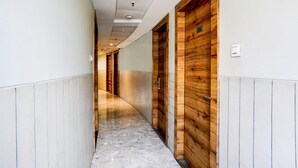 Un couloir avec des portes en bois, des murs blancs et un sol en marbre.