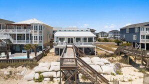 A beachfront property with multiple buildings, a swimming pool, and a wooden deck leading to the beach. - Chasing Sunrises | Newly Rebuilt Luxury Oceanfront Retreat (Ocean Isle Beach)